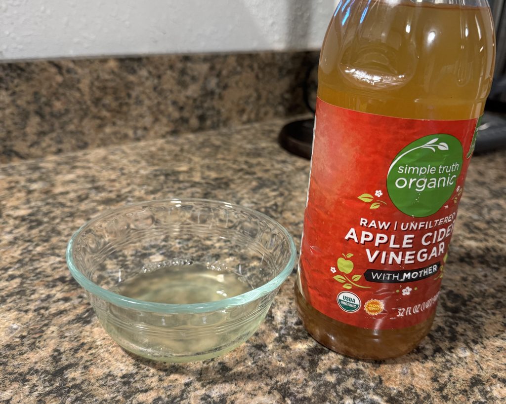 A homemade fruit fly trap consisting of apple cider vinegar and soap in a small glass bowl.