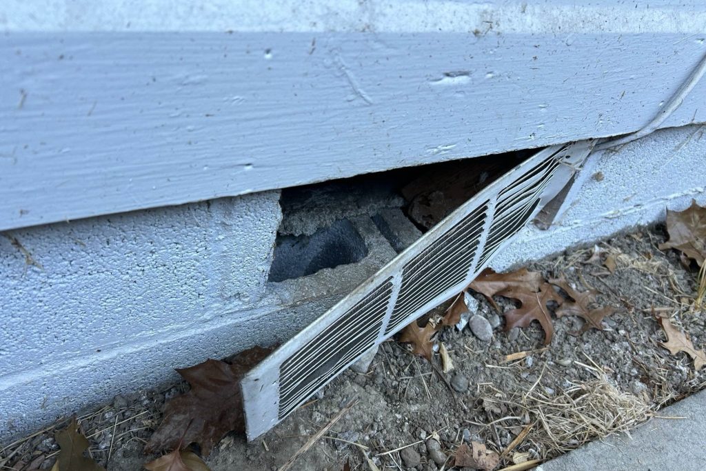 A broken foundation vent on a home’s exterior, leaving a gap that rodents or wildlife could use to enter.